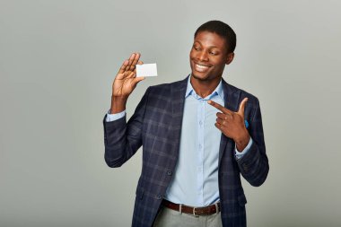 Zarif takım elbiseli yakışıklı Afro-Amerikan işadamı gri bir fona karşı zarafetle bir kartvizit uzatıyor..