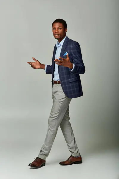 stock image African American businessman in checkered blazer walking purposefully in formal attire on grey background.