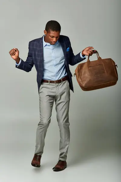 stock image A dapper African American man in a checkered blazer holding a brown bag against a grey backdrop.