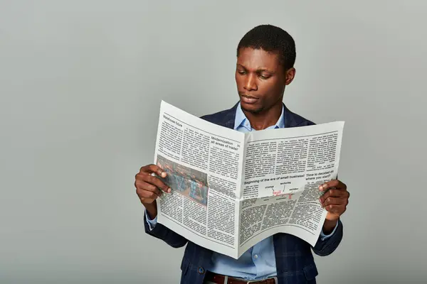 stock image Stylish African American businessman in checkered blazer, fully immersed in reading a classic newspaper.