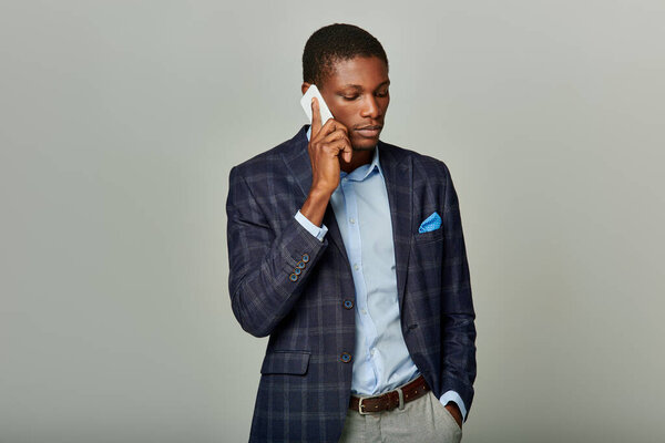 A young African American businessman in a checkered blazer is engaged in a phone conversation, exuding professionalism.