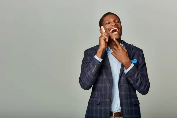 Stock image An African American businessman in a checkered blazer suit talking on a cellphone against a grey backdrop.