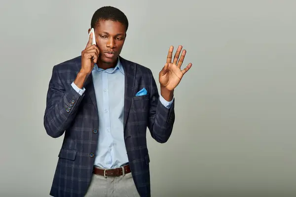 Stock image Young African American businessman in checkered blazer talking on cell phone against grey backdrop.