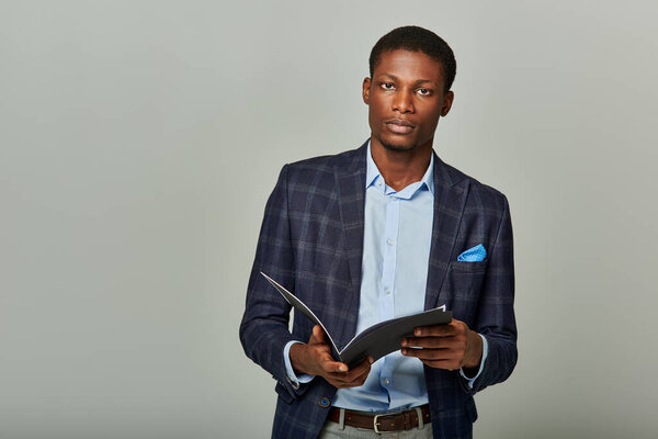 African American man in checkered blazer holds a folder, exuding professionalism in a formal business setting.