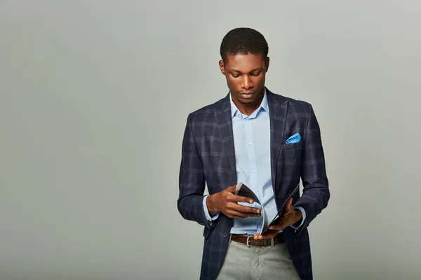 stock image African American businessman in checkered blazer gazes at his folder on grey background.