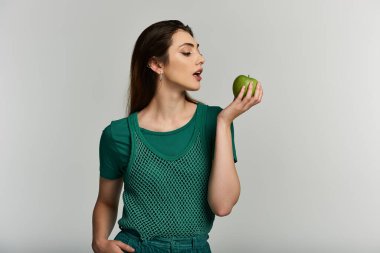 Yeşil gömlekli ve pantolonlu genç bir kadın elinde yeşil bir elma tutuyor..