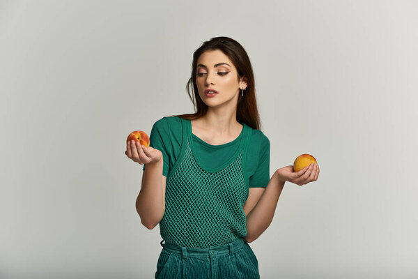 A young woman in a green top holds two peaches in her hands, contemplating her choice.