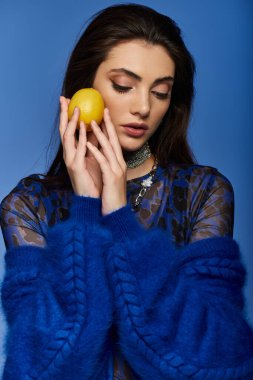 Mavi kazaklı genç bir kadın yanağına limon tutuyor..