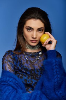Mavi ve siyah hayvan desenli tişörtlü genç bir kadın yüzüne bir limon tutuyordu..