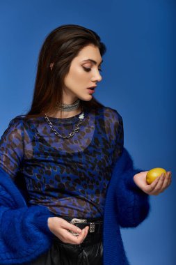 Mavi desenli bluzlu genç bir kadın mavi arka planda bir limon tutuyor..