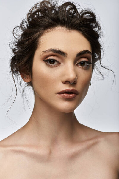 Portrait of a young woman with dark updo, minimal makeup, and a nose ring.