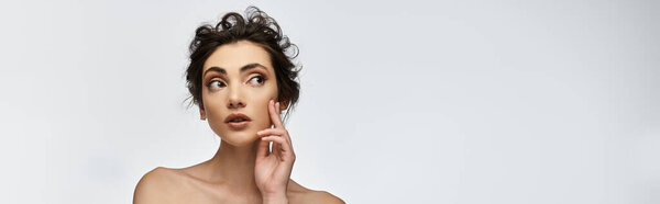 A young woman with dark hair and a piercing stares thoughtfully off to the side.
