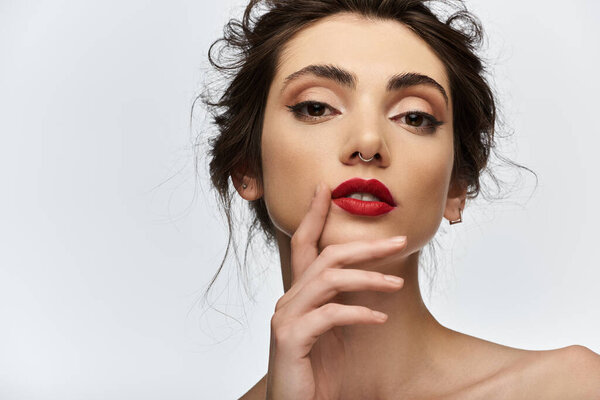 A woman with red lipstick and a nose ring looks directly at the camera.