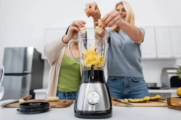 Low angle view of blurred friends putting banana in blender in kitchen — Stock Photo