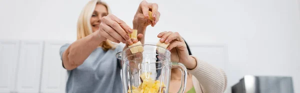 Vue à angle bas des amis flous mettant des fruits dans le mélangeur, bannière — Photo de stock