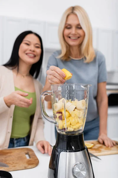 Desfocado interracial mulheres fazendo fruta smoothie na cozinha — Fotografia de Stock