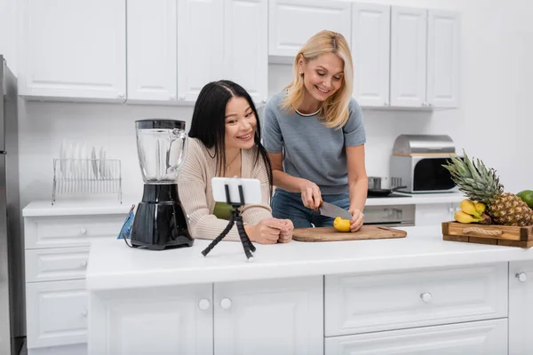 Multiethnic bloggers cutting lemon near smartphone on tripod in kitchen — Stock Photo