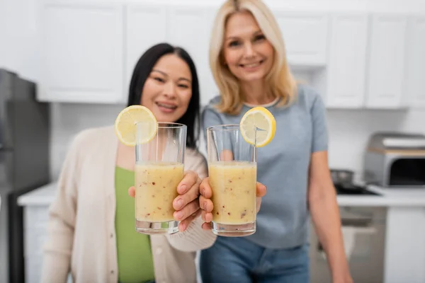 Blurred multiethnic women holding glasses of smoothie at home — Stock Photo