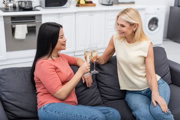 Amici interrazziali che parlano mentre tengono bicchieri di champagne sul divano a casa — Foto stock