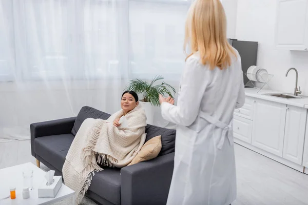 Disiased asiatique femme en couverture en regardant flou médecin à la maison — Photo de stock