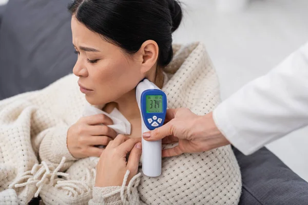 Médico midiendo temperatura de enfermo asiático paciente en casa - foto de stock