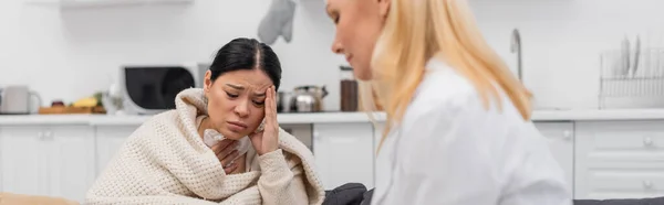 Kranke asiatische Frau leidet unter Kopfschmerzen in der Nähe verschwommener Arzt zu Hause, Banner — Stockfoto