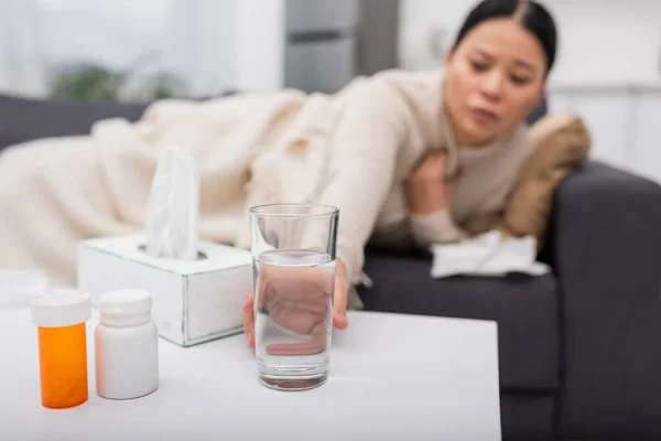 Blurred woman taking glass of water near pills and napkins at home — Stock Photo