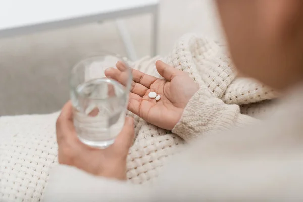 Cropped view of woman holding glass of water and pills at home — Stock Photo