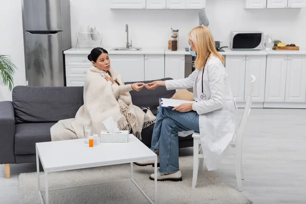 Enfermo asiático mujer dando termómetro a médico en médico máscara en casa — Stock Photo