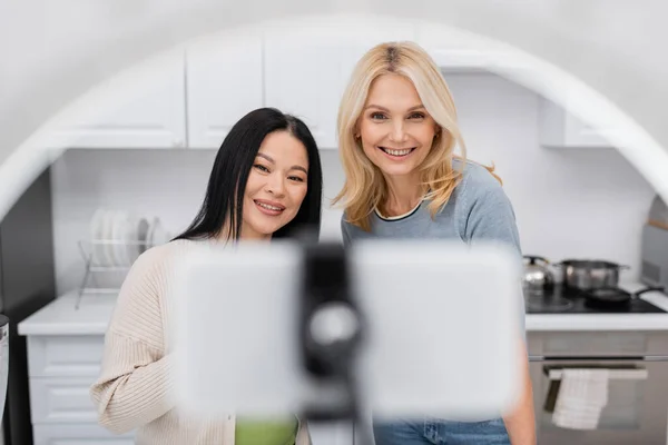 Alegre interracial bloggers mirando borrosa smartphone en anillo lámpara en casa - foto de stock