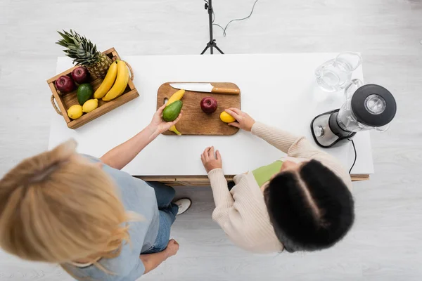 Overhead view of friends holding fruits near blender in kitchen — Stock Photo