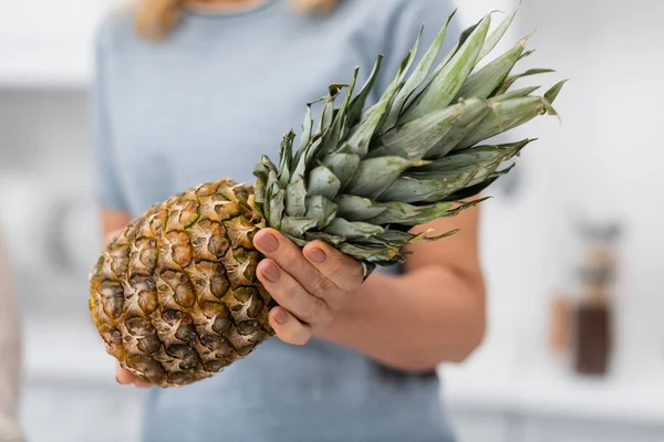 Cropped view of blurred woman holding ripe pineapple at home — Stock Photo