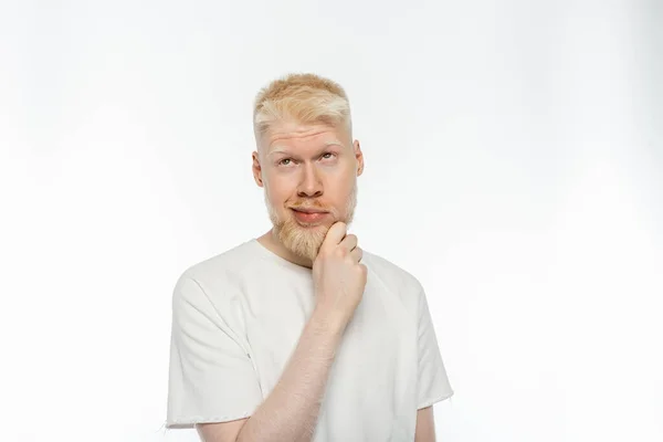 Pensoso albino uomo in t-shirt toccare la barba mentre si pensa su sfondo bianco — Foto stock