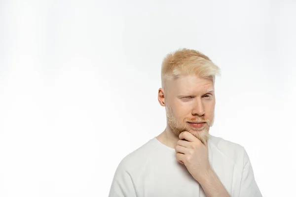 Задумчивый альбинос трогает бороду, думая на белом фоне — стоковое фото