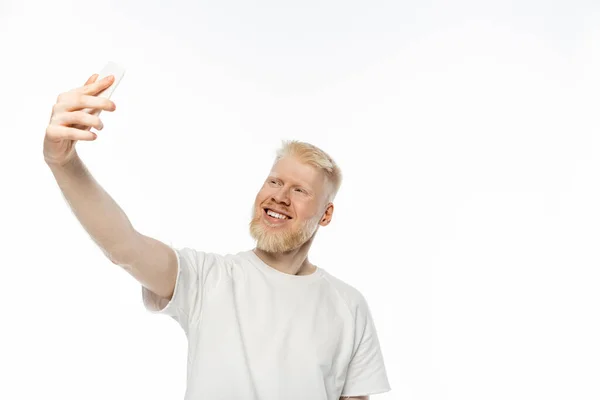 Cheerful albino man in t-shirt taking selfie on smartphone on white background — Stock Photo