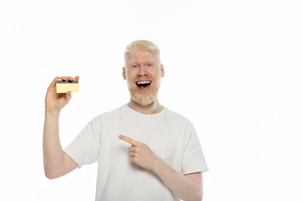 Uomo albino stupito in t-shirt che punta sulla carta di credito isolata su bianco — Stock Photo