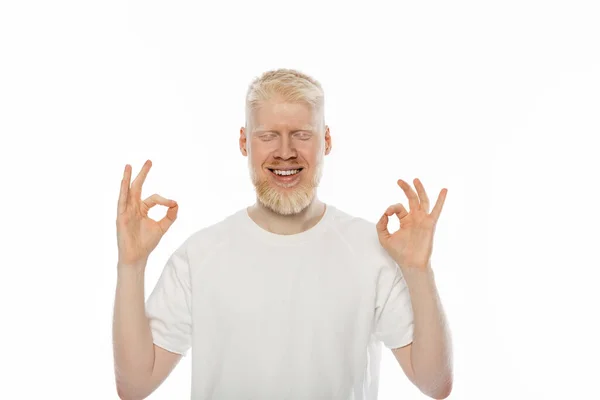 Hombre albino alegre con los ojos cerrados mostrando signo ok con las manos aisladas en blanco - foto de stock