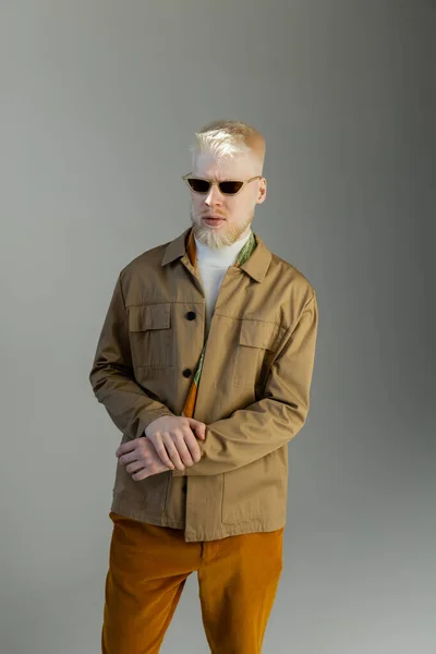 Elegante uomo albino in occhiali da sole e giacca camicia in piedi isolato su grigio — Foto stock