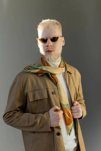 Sunlight on face of stylish albino model in sunglasses and shirt jacket isolated on grey — Stock Photo