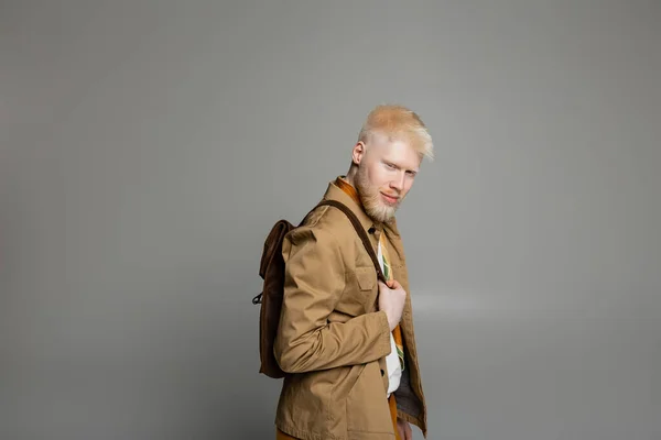 Bearded albino man in stylish shirt jacket and silk scarf posing with backpack isolated on grey — Stock Photo