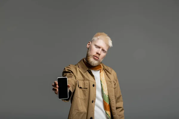 Hombre albino barbudo en chaqueta de camisa que sostiene el teléfono inteligente con pantalla en blanco aislado en gris - foto de stock