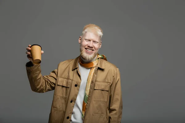 Bearded and happy albino man in shirt jacket holding paper cup isolated on grey — Stock Photo