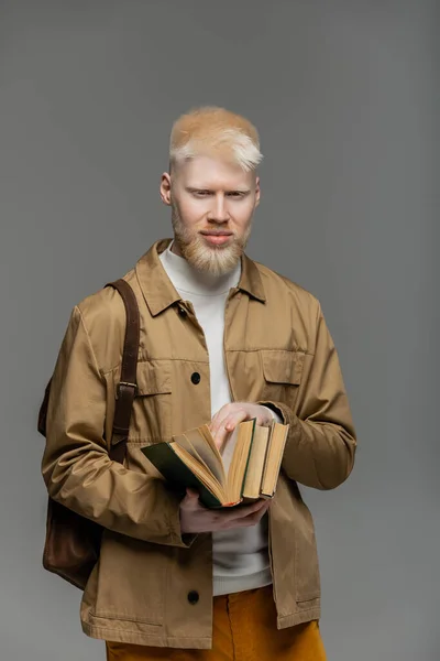 Bearded albino man with backpack holding books isolated on grey — Stock Photo