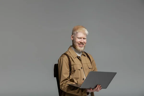 Щасливий студент альбіносу з рюкзаком за допомогою ноутбука під час вивчення онлайн ізольовано на сірому — стокове фото