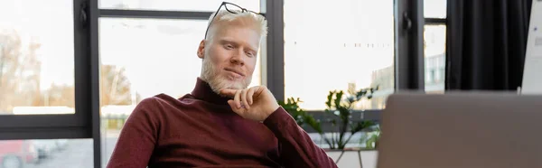 Pensive albino businessman in glasses looking at laptop in office, banner — Stock Photo