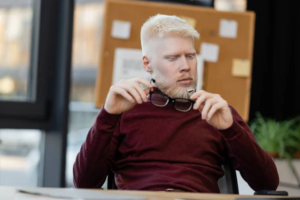 Homme d'affaires barbu albinos tenant des lunettes tout en pensant au bureau — Photo de stock