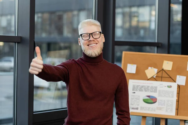 Бородатый бизнесмен-альбинос в очках улыбается и показывает большой палец в офисе — стоковое фото