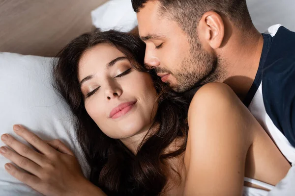 Бородатий чоловік цілує красиву дівчину брюнетку в спальні — стокове фото