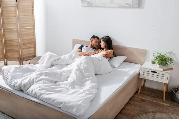 Bearded man hugging brunette girlfriend on bed at home — Stockfoto