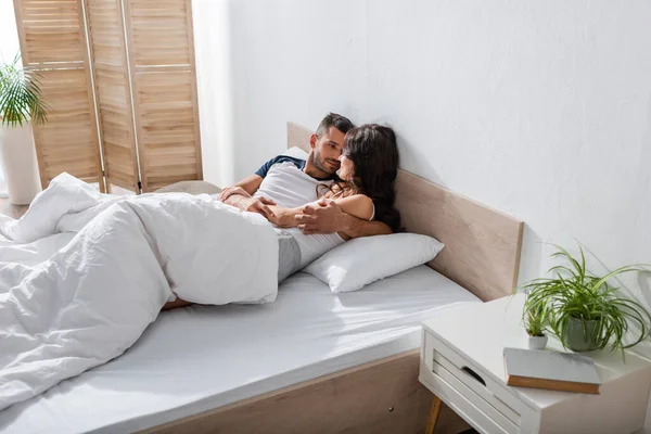 Bärtiger Mann umarmt Freundin im Pyjama beim Entspannen auf dem Bett — Stockfoto